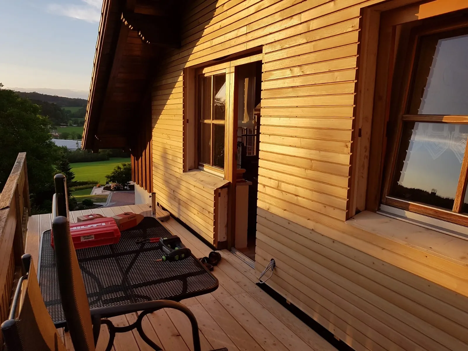 Neue Holzverschalung und Terrassenboden an einem Haus im Abendlicht, im Hintergrund Wiesen und Wald